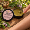 One fingertip taking comfrey leaf paste from a shallow tin
